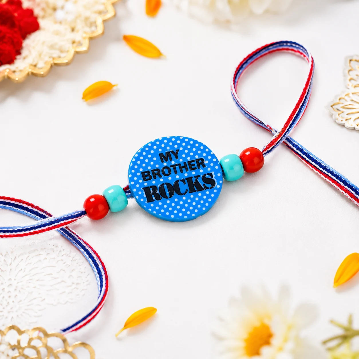 A playful blue polka-dot rakhi with "My Brother Rocks" text, paired with colorful striped threads for a fun festive look.